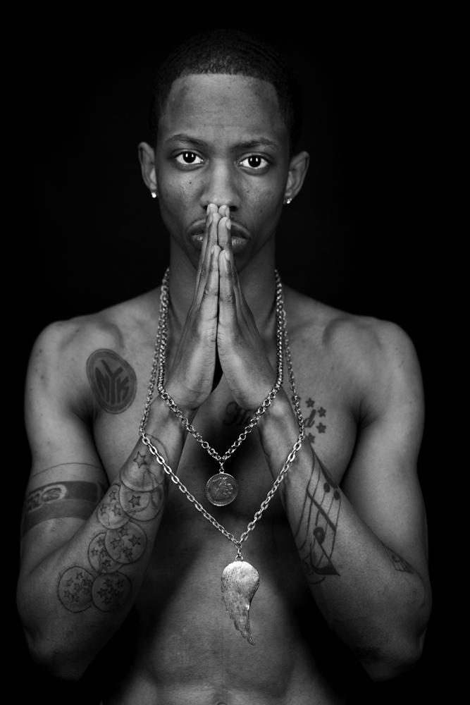 ﻿Man with tattoos looking into camera with necklaces around his hands